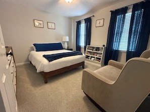 Um quarto com cama, cadeira, estante e cômoda.