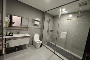 A modern bathroom with a glass-enclosed shower, a white toilet, and a vanity with a mirror and towel rack. - Linlong Hotel in Yinjiang (Yinjiang)