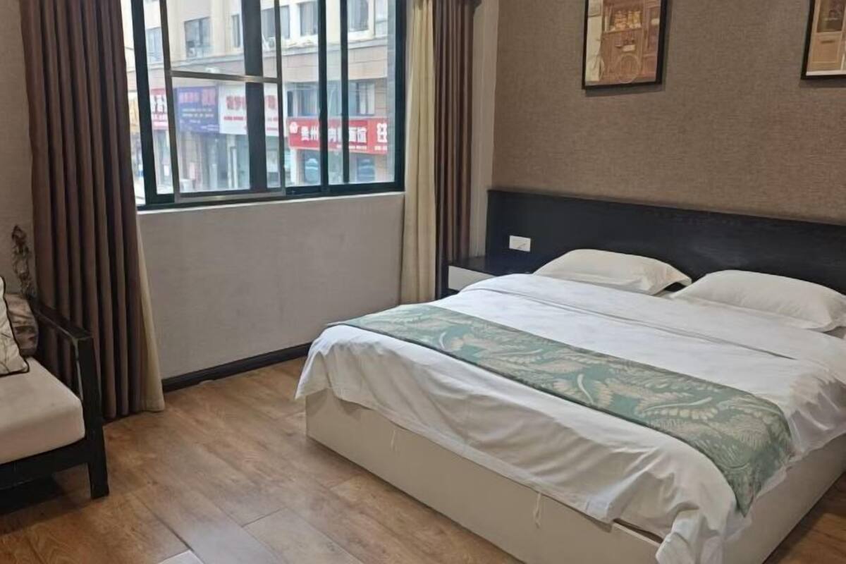 A hotel room with a bed, a chair, a window, and a wall with framed pictures.