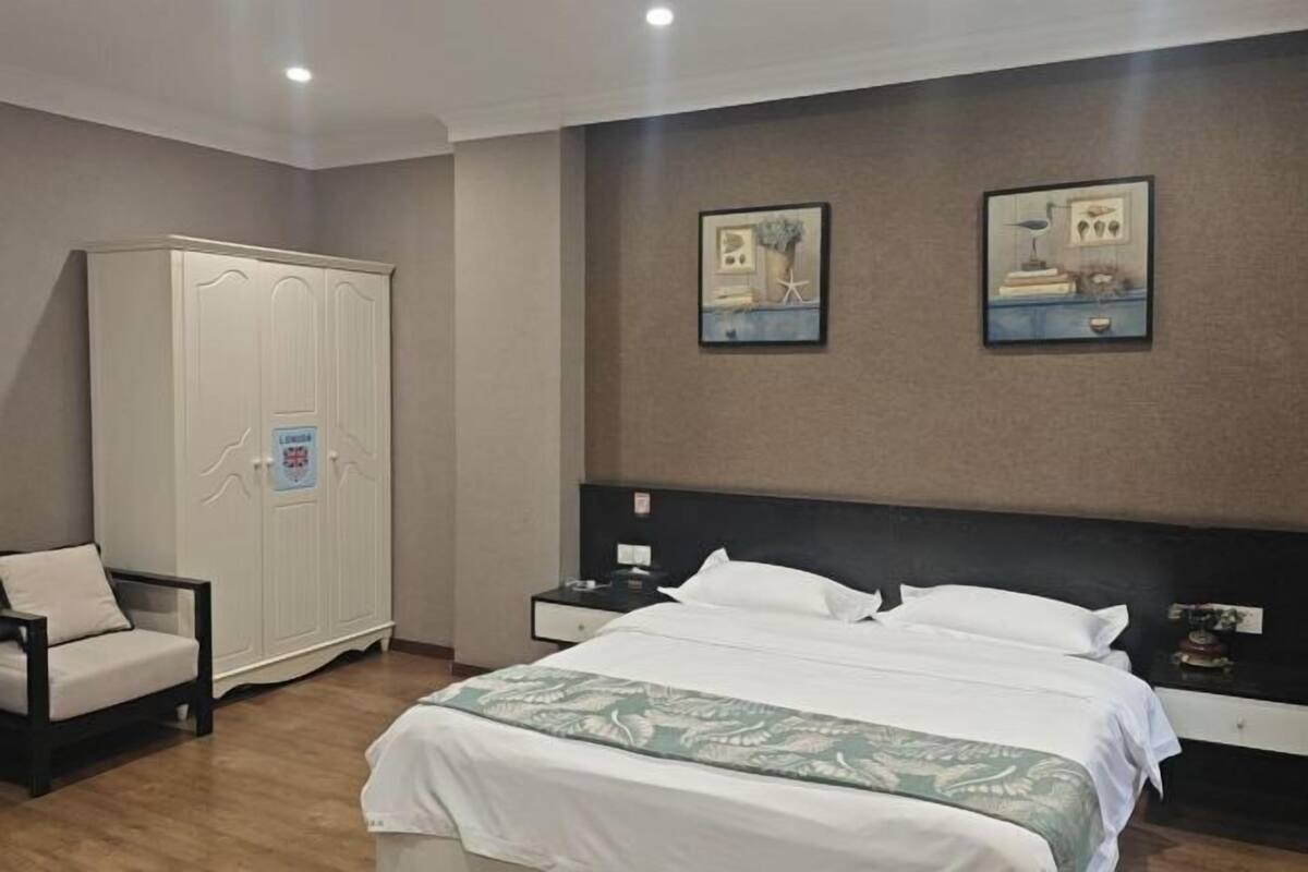 A bedroom with a bed, nightstands, a wardrobe, a chair, and two framed pictures on the wall.