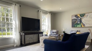 A living room with a large flat-screen TV, a blue sofa, a patterned armchair, and a painting on the wall.