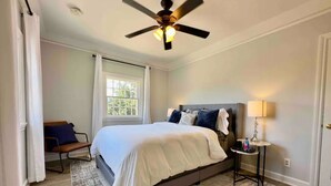 A bedroom with a bed, a nightstand, a ceiling fan, a window, and a door.