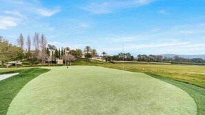 A golf course with a well-maintained green, a flagstick, and a distant building.