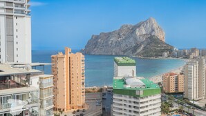 Un paisaje costero con modernos rascacielos, una montaña destacada y una playa.