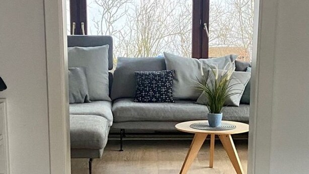 Ein modernes Wohnzimmer mit einem grauen Sofa, einem runden Holztisch und einer Topfpflanze.
