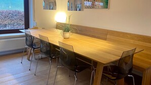 Ein moderner Essbereich mit Holztisch, transparenten Stühlen, einer Topfpflanze, Pendelleuchten und einem großen Fenster mit Blick aufs Meer.