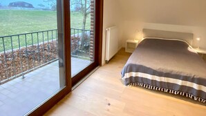 Ein Schlafzimmer mit großem Fenster, einem Bett mit gestreifter Decke, einem Nachttisch und einem Heizkörper.