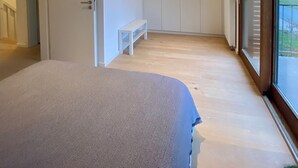 Ein Schlafzimmer mit einem Bett, einer Bank, einem Kleiderschrank und einer Schiebetür zu einem Balkon.