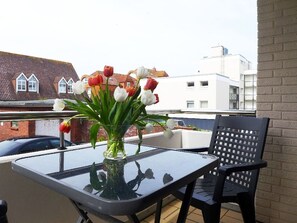 Un balcone con un tavolo in vetro e una sedia, un vaso con fiori, e edifici sullo sfondo.