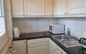 Una cucina con mobili bianchi, un piano di lavoro nero, un forno a microonde, un lavello e un espositore per piatti.