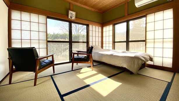 A traditional Japanese-style room with tatami flooring, a bed, two chairs, and large windows. - Nodoka (Nikko)