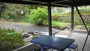 A covered outdoor area with a table and chairs, surrounded by a garden with rocks and plants. - Nodoka (Nikko)