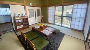 A traditional Japanese room with tatami flooring, a low wooden table with cushions, a wooden cabinet with glass doors, and sliding doors with a view of greenery outside. - Nodoka (Nikko)