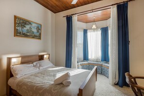 Een slaapkamer met een bed, een stoel, een raam met gordijnen en een schilderij aan de muur.