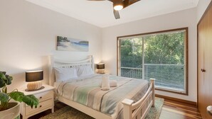 A bedroom with a bed, bedside lamps, a ceiling fan, a window with blinds, and a painting on the wall. - Gillmith - Sleeping up to 16 people (Pambula Beach)