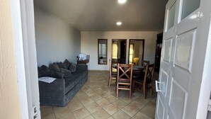 A living area with a sofa, dining table, chairs, and a mirror.