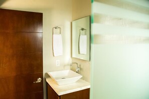 A bathroom with a wooden door, a white sink, and a mirror with a towel hanging on the wall.