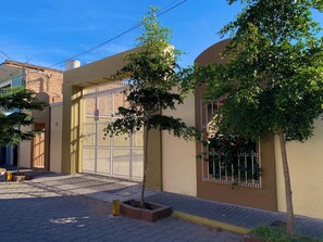 A residential building with a gated entrance, a small tree in a planter, and a paved driveway.