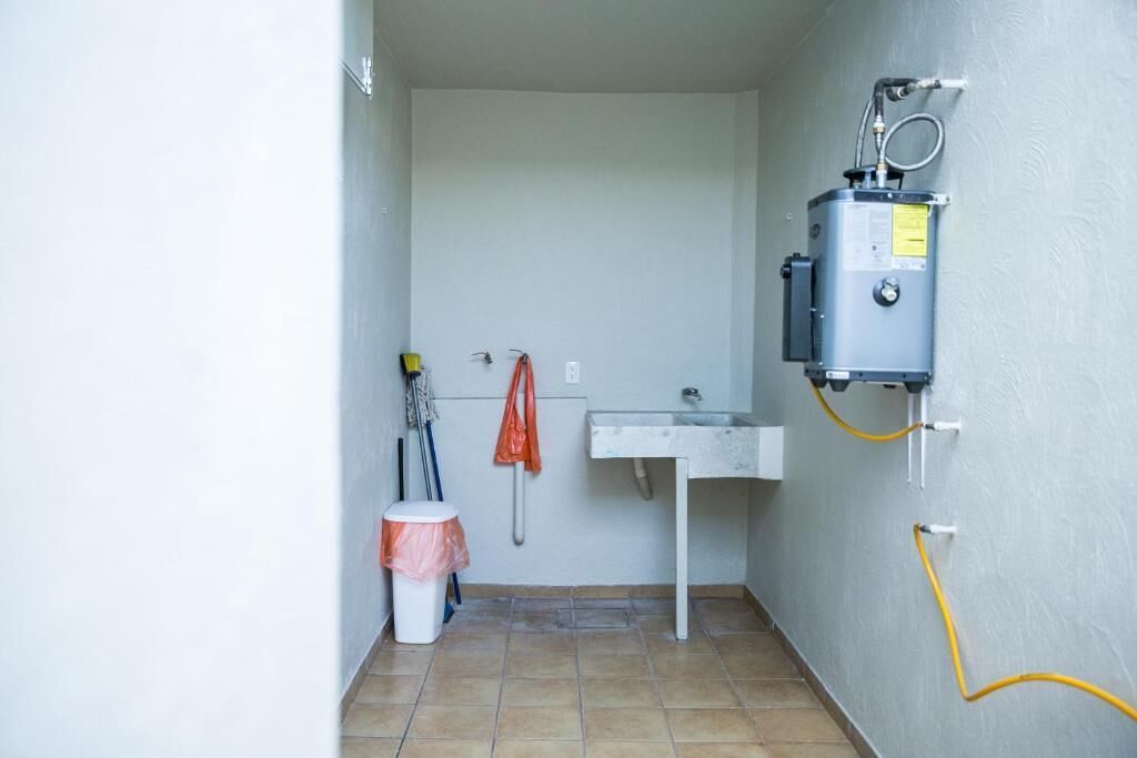 A small bathroom with a white sink, a toilet, and a shower. There are cleaning supplies and a yellow hose on the wall.