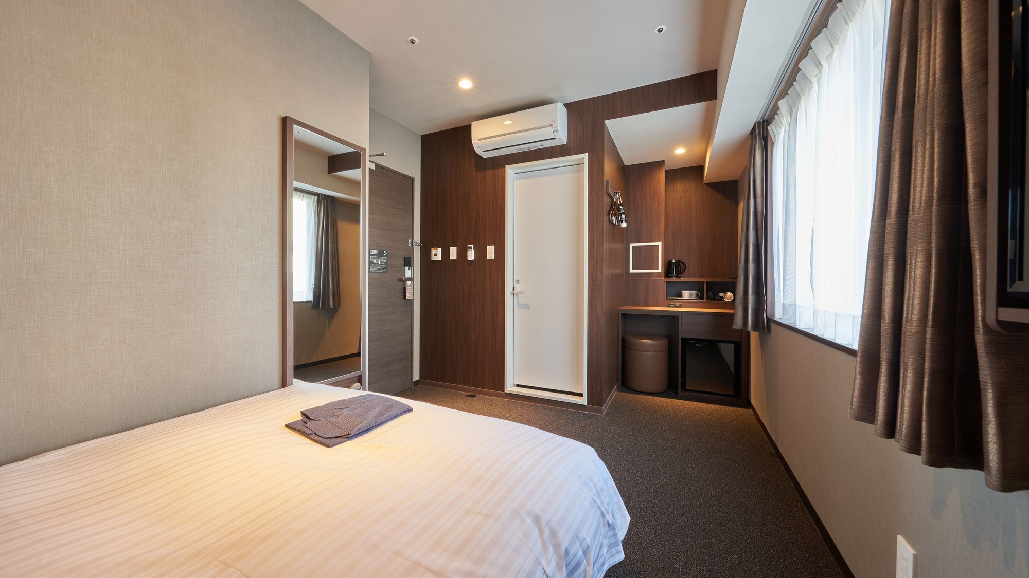 A hotel room with a bed, a small kitchenette, a bathroom, and a mirror.