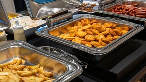 Ein Buffet mit verschiedenen Speisen, darunter gebratenes Hähnchen, Würstchen und Kartoffelspalten.