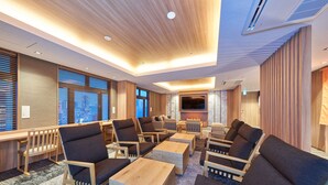 Un moderno vestíbulo de hotel con mobiliario de madera, un televisor de pantalla plana y ventanas amplias con persianas.