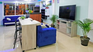 Vestíbulo de hotel con mostrador de recepción, zona de estar, televisor y plantas en macetas.