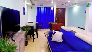 Un hall de hotel con un sofá azul, una mesa de madera, una mesa de fútbol de mesa, un televisor y una planta en maceta.