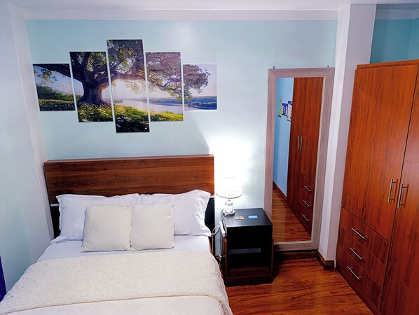 Un dormitorio con cabecera de madera, cama con ropa de cama blanca, mesita de noche con lámpara y armario.