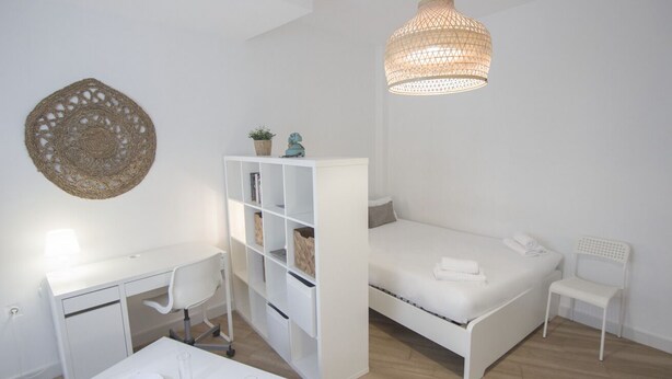 A minimalist bedroom with a white desk, a bed, a white chair, and a hanging light fixture. - Rentalsevilla Living La Alameda (Sevilla)