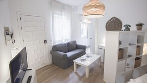 A modern living room with a grey sofa, white coffee table, and a white shelving unit. - Rentalsevilla Living La Alameda (Sevilla)