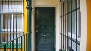 A black door with a brass doorknob, flanked by green railings and a yellow wall. - Rentalsevilla Living La Alameda (Sevilla)