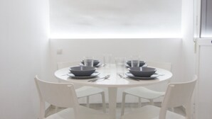 A round dining table with white chairs, set with dark bowls and clear glasses. - Rentalsevilla Vive el Salvador (Sevilla)
