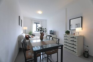 A compact living space with a dining area, a sofa, a TV, and a white cabinet with drawers.