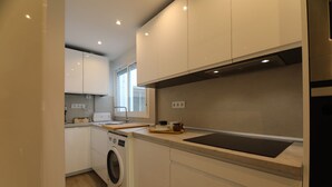 A compact kitchen with white cabinets, a washing machine, and a countertop with a sink. - Rentalsevilla 3 Dormitorios Junto a la Macarena (Sevilla)