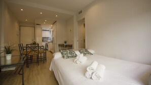 A hotel room with a large bed, a dining table with chairs, a small kitchen area, and a hallway leading to another room. - Rentalsevilla 3 Dormitorios Junto a la Macarena (Sevilla)