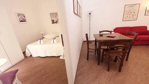A compact living space with a dining area, a red sofa, and a bed with a white cover.