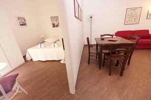 Um espaço de estar compacto com área de refeições, um sofá vermelho e uma cama com cobertura branca.