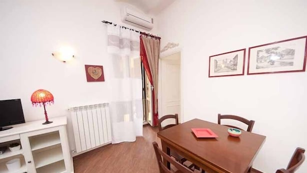 A dining area with a wooden table and chairs, a white cabinet with a television, and a radiator.