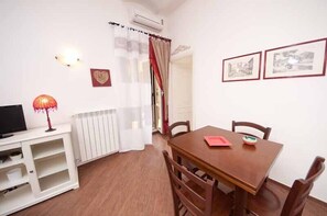 A dining area with a wooden table and chairs, a white cabinet with a television, and a radiator.