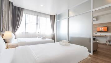 Habitación de hotel con dos camas, un escritorio, un televisor y una ventana con cortinas.