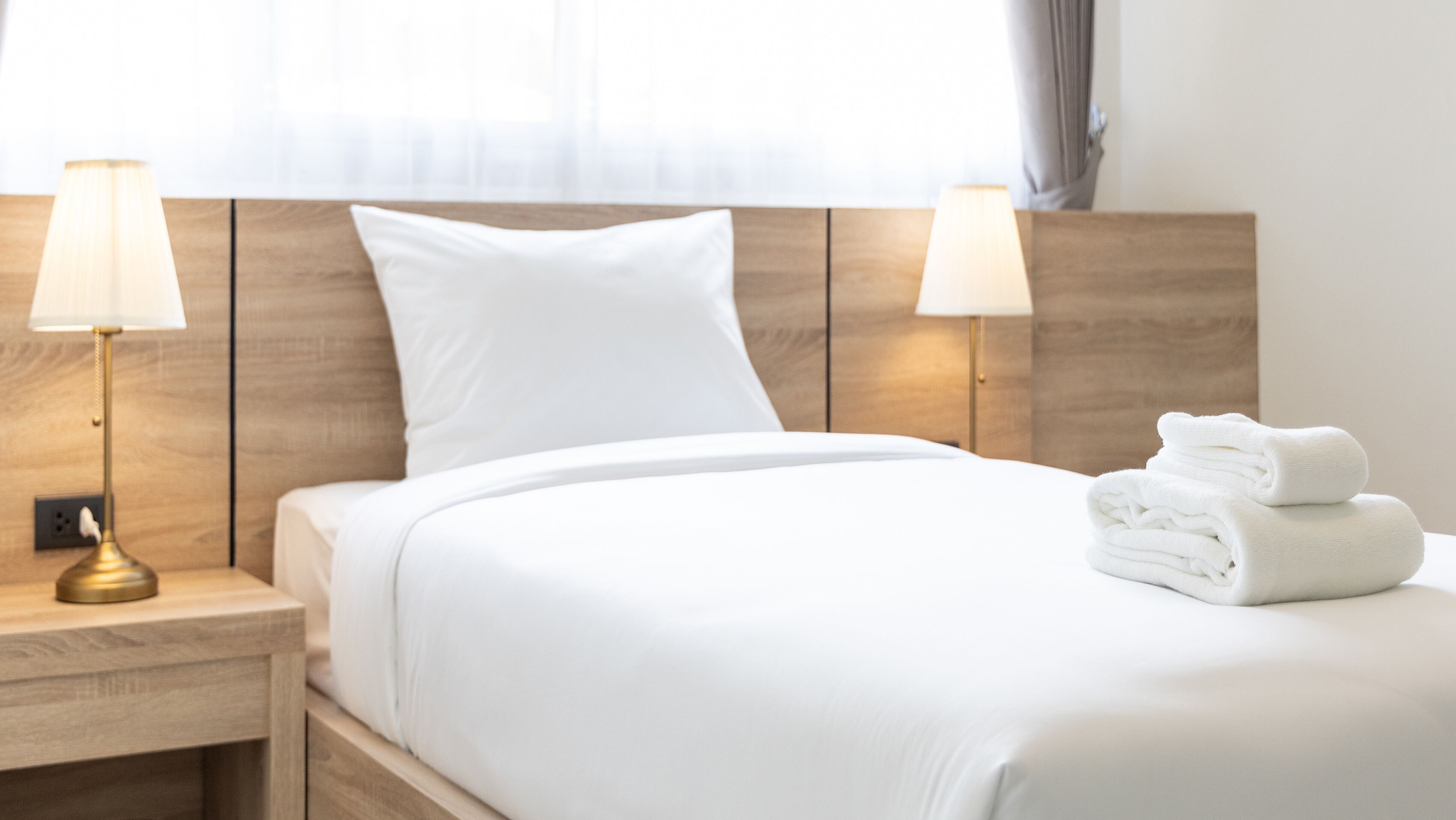 A neatly made bed with white linens, two bedside lamps, and a stack of folded towels on the nightstand.