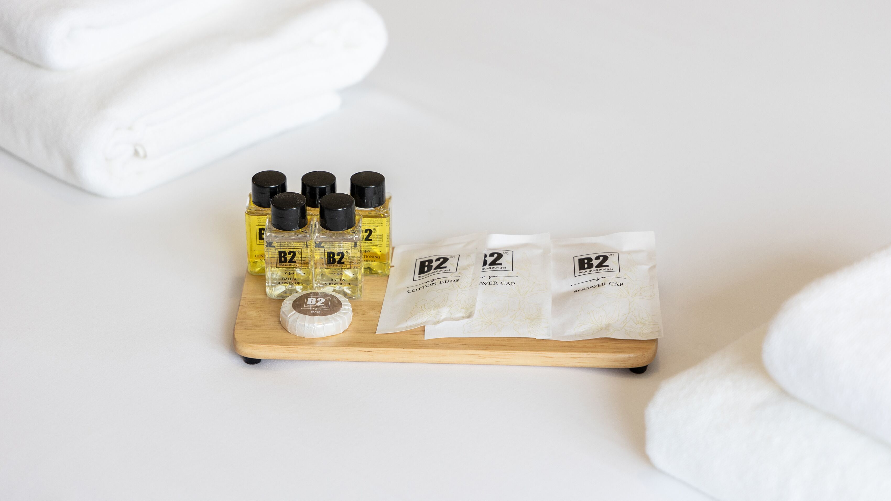 A wooden tray with B2 bath products, including cotton buds and shower cap, on a white surface.