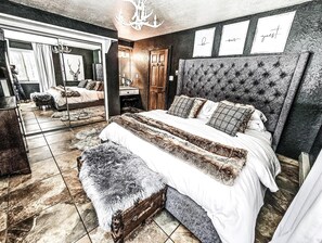A bedroom with a large bed, a mirror, a chandelier, and framed text on the wall. - Luxury Angel Fire Retreat - Fireplace, Skiing & Mountain Charm (Angel Fire)
