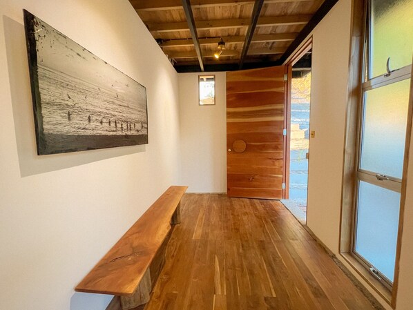 Un pasillo con un banco de madera, una puerta de madera y una obra de arte enmarcada en la pared.