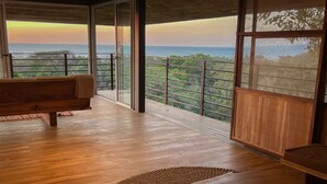 Un'ampia stanza con pavimento in legno, un'ampia finestra con vista sull'oceano e sul verde, e una panca.