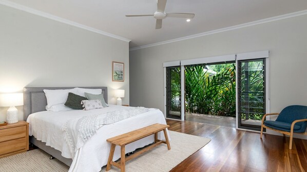 A bedroom with a bed, bedside tables, a bench, a chair, and a view of greenery through a sliding door.