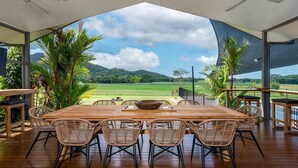Une terrasse en bois avec une table et des chaises, donnant sur un paysage verdoyant, avec des arbres et un ciel dégagé.