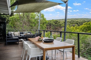 A wooden deck with outdoor furniture, a table, and a large umbrella providing shade.