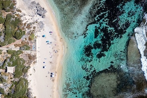 An aerial view of a beach with clear turquoise waters, sandy shore, and several beach umbrellas.